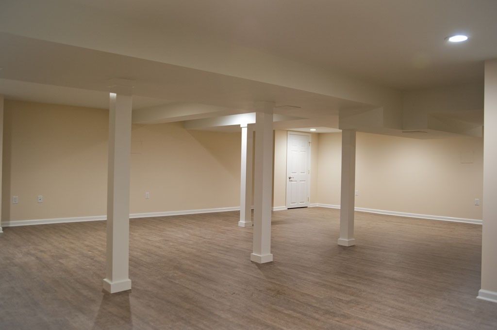 Empty finished basement with carpet, support beams, and a white door.