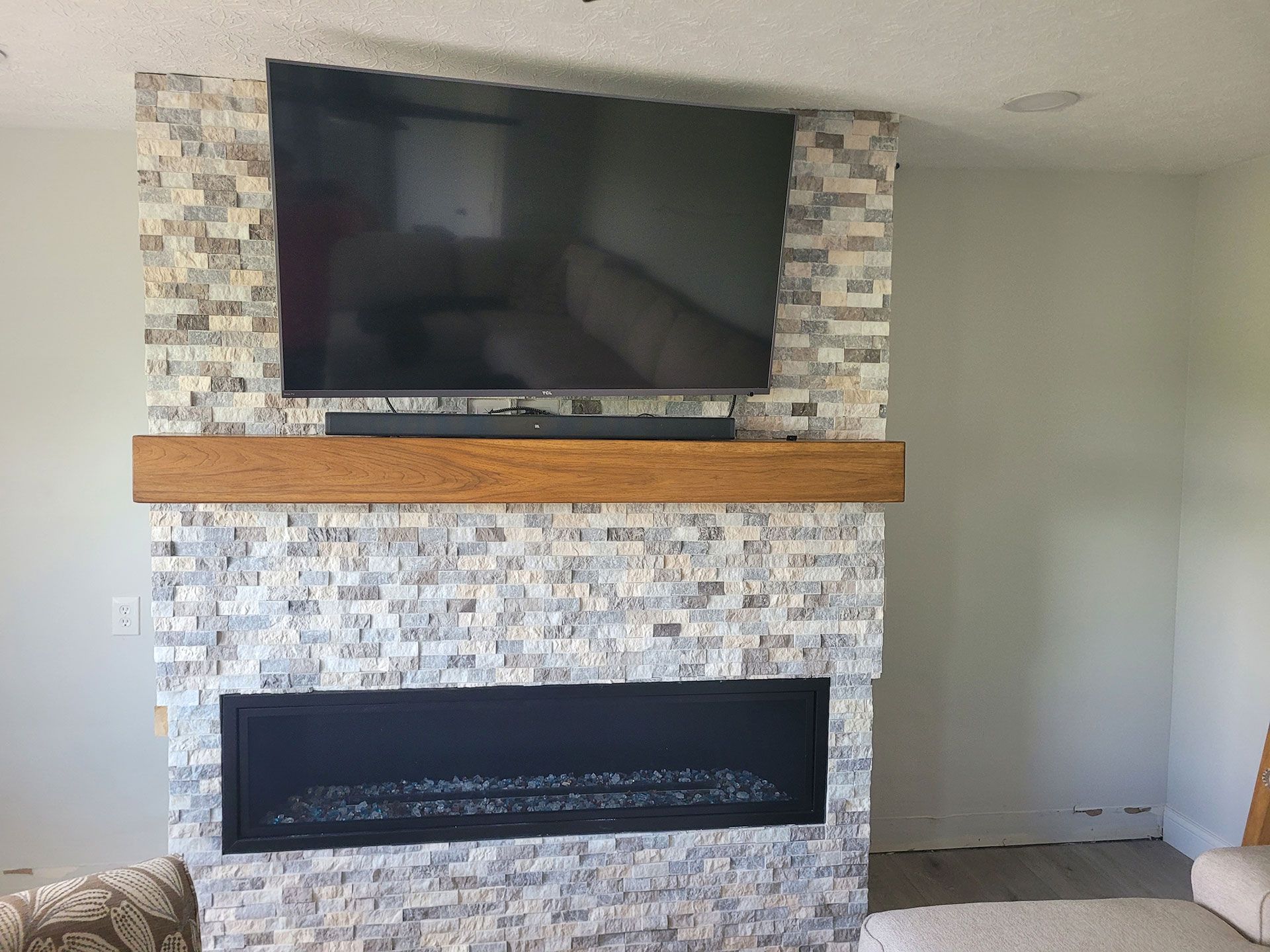 TV mounted above a fireplace with stone tile and a wooden mantel.