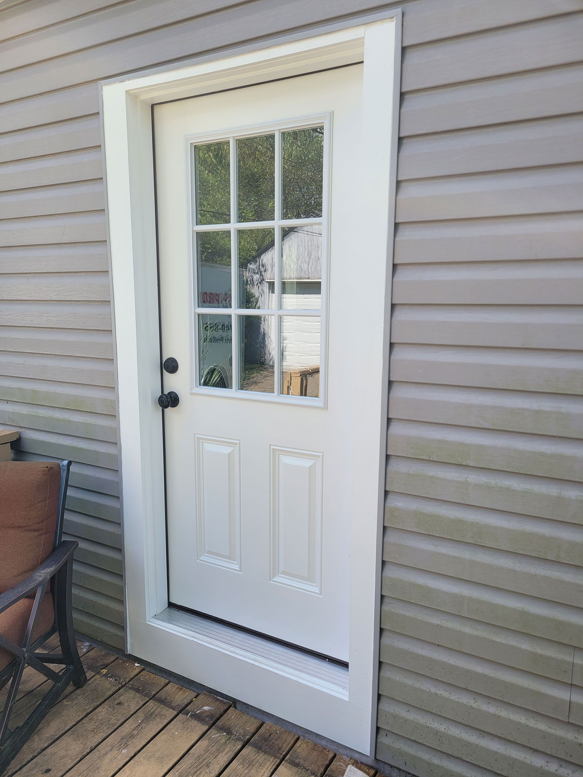 White exterior door with glass panes, framed in white trim, set in gray siding.
