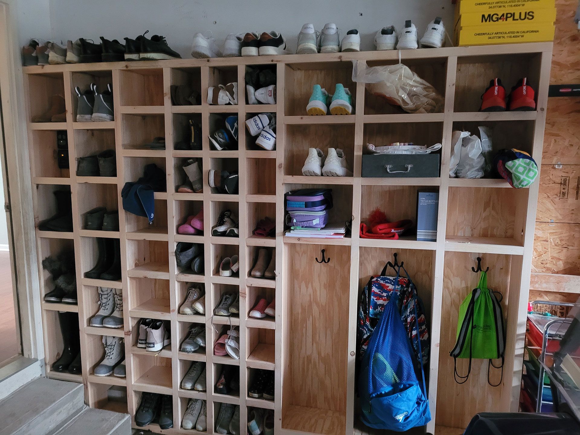 Wooden shoe organizer filled with various shoes and boots. Includes coat hooks with bags.