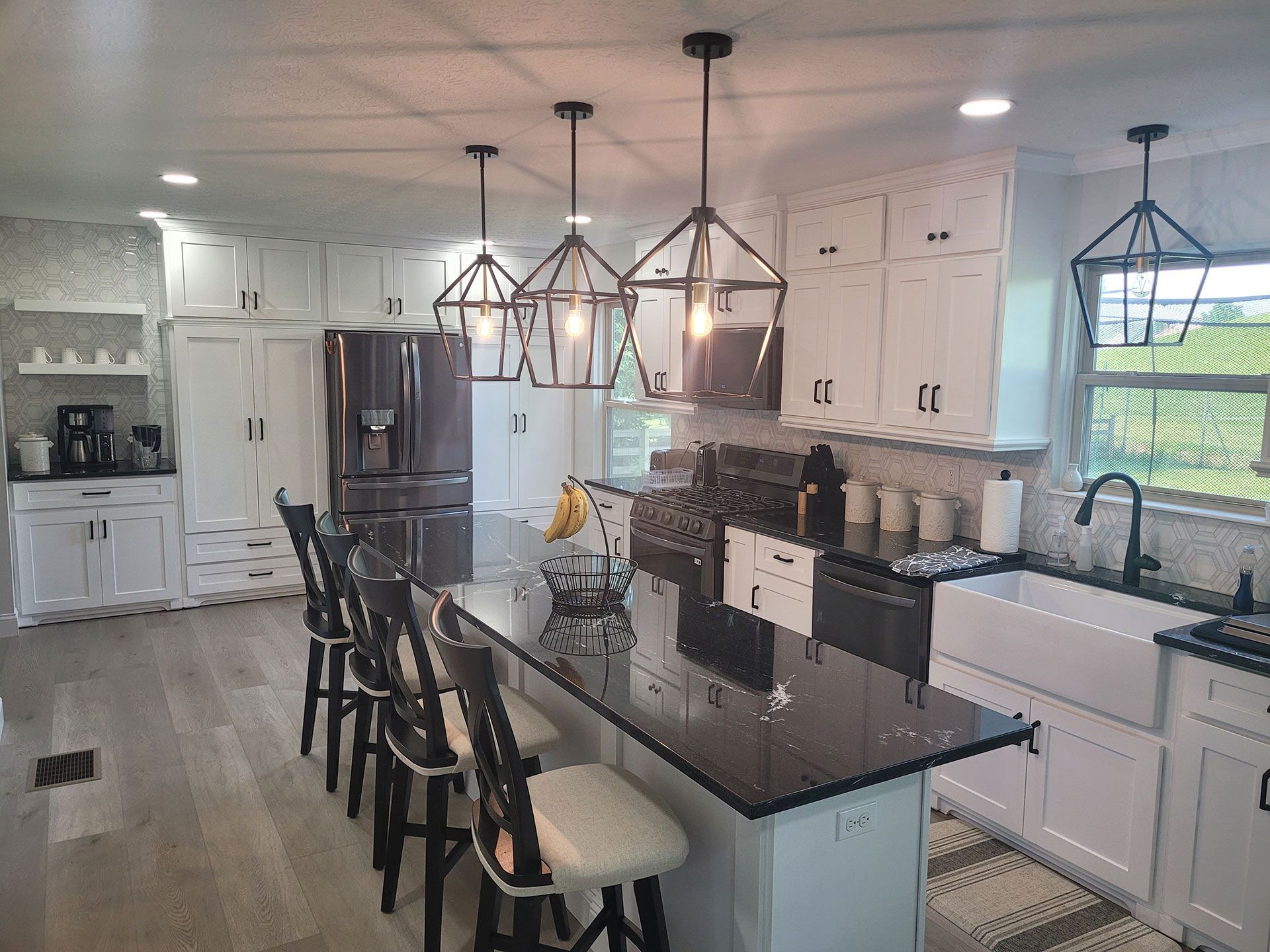 Modern kitchen with white cabinets, black island with stools, and geometric pendant lights.