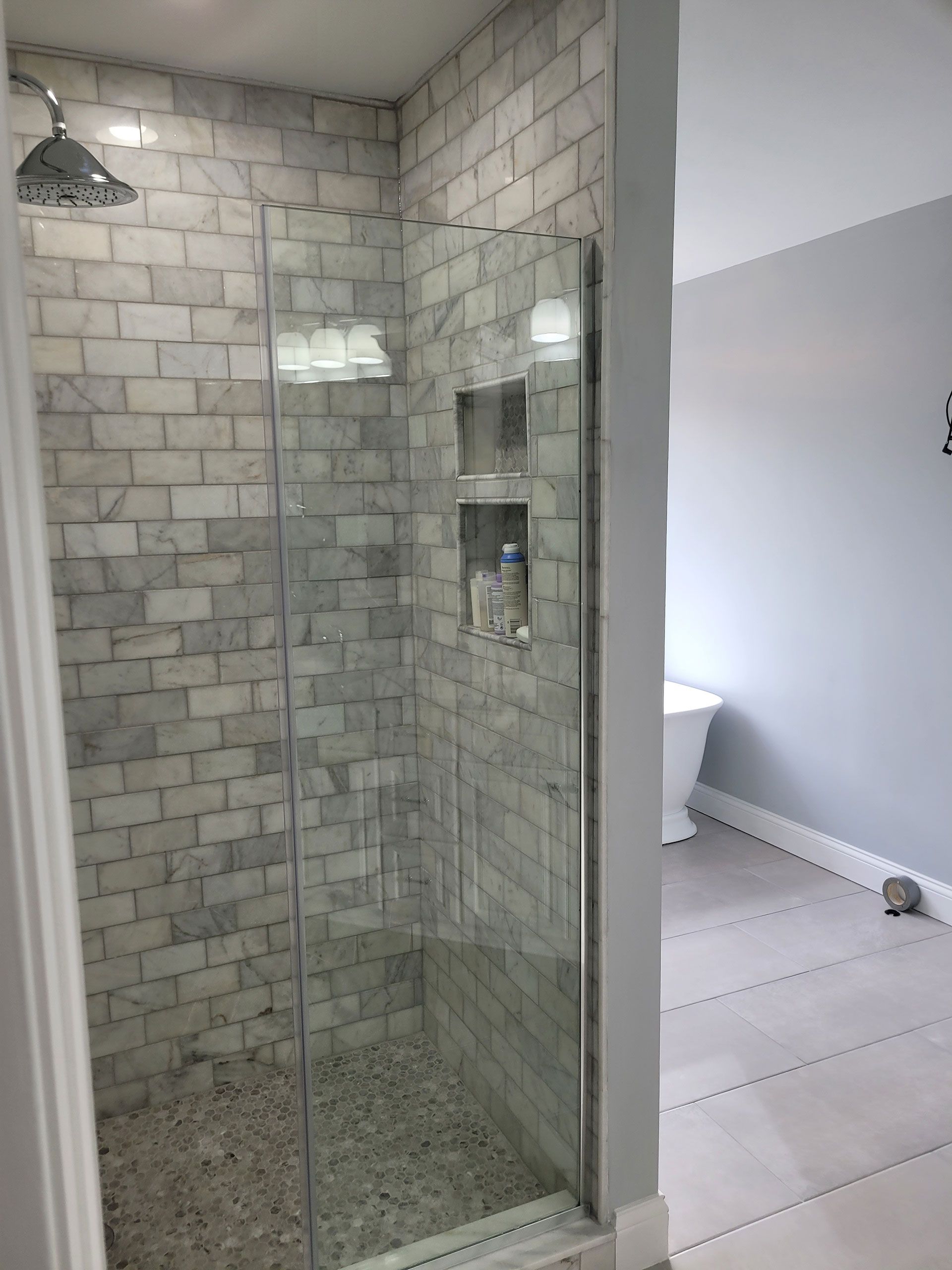 Shower stall with marble brick-style tiles, glass doors, and built-in shelving.