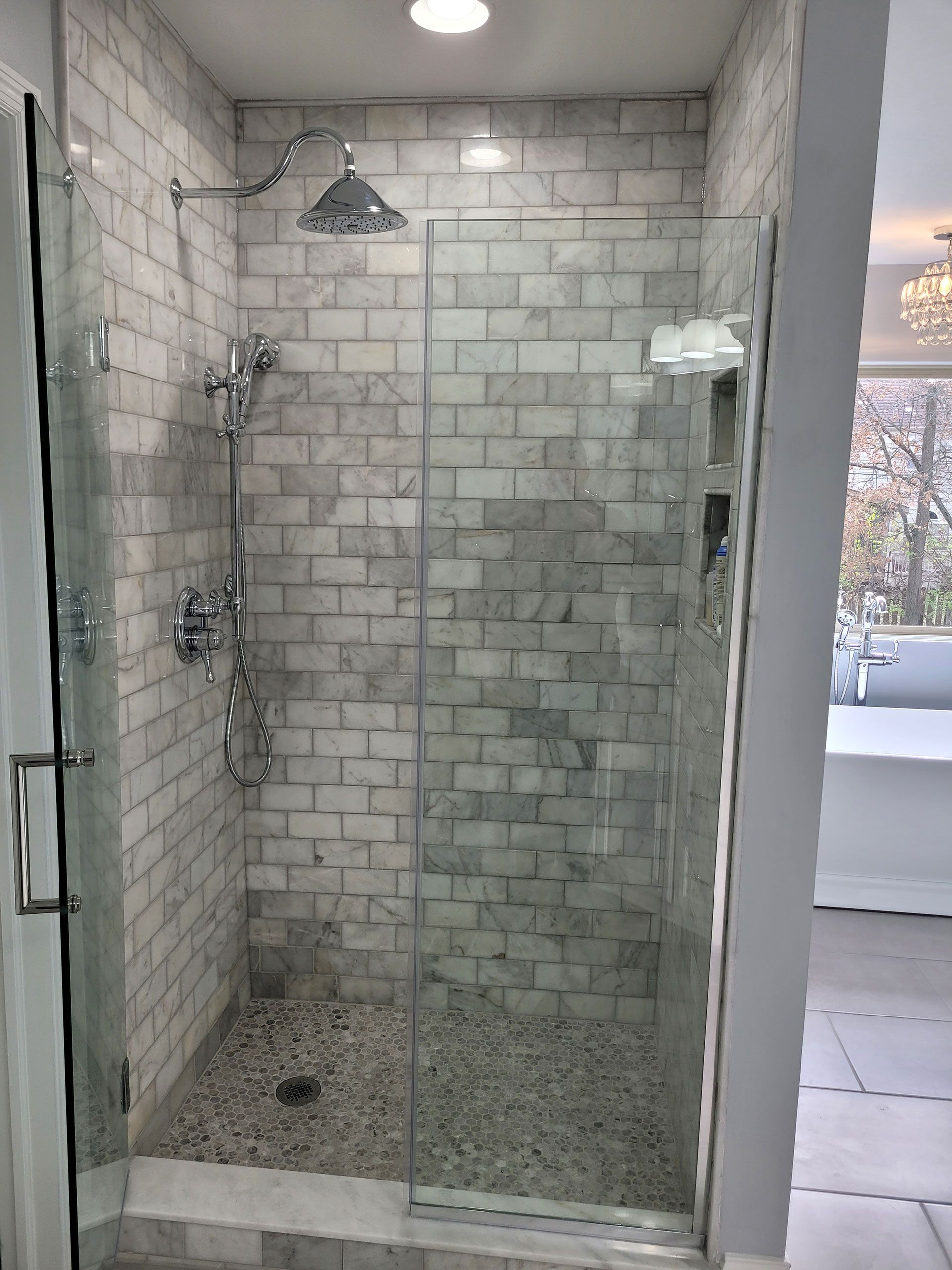 Shower with glass doors and pebble floor; marble brick-style tiles on walls.