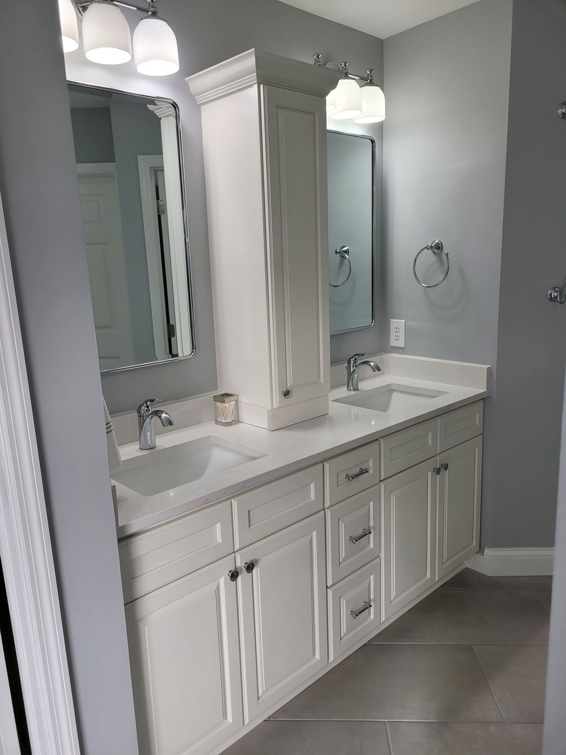 Bathroom with white vanity, double sinks, and a tall cabinet; gray walls.