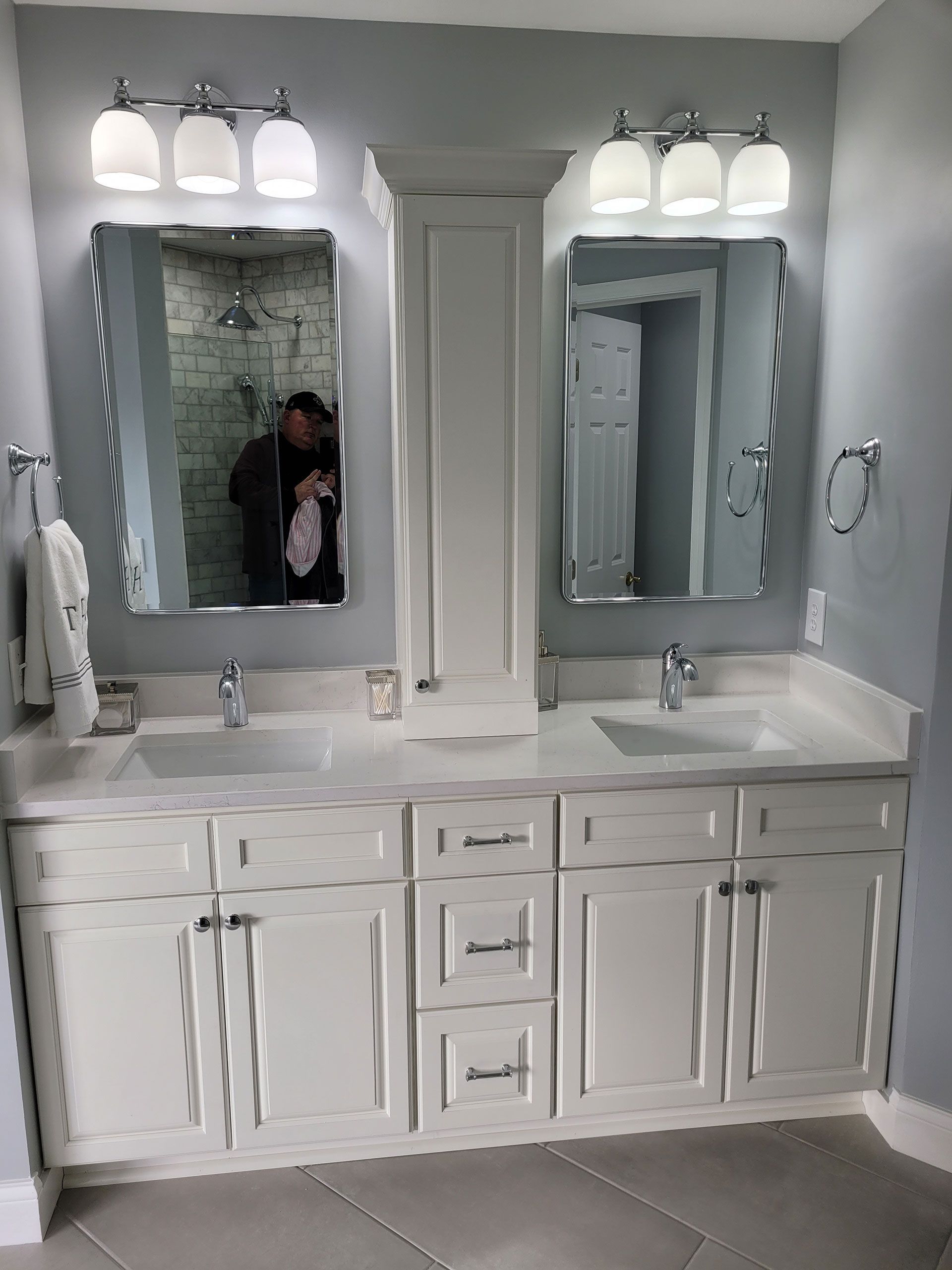Bathroom with two sinks, white cabinets, mirrors, and light fixtures. Gray walls, light countertop.