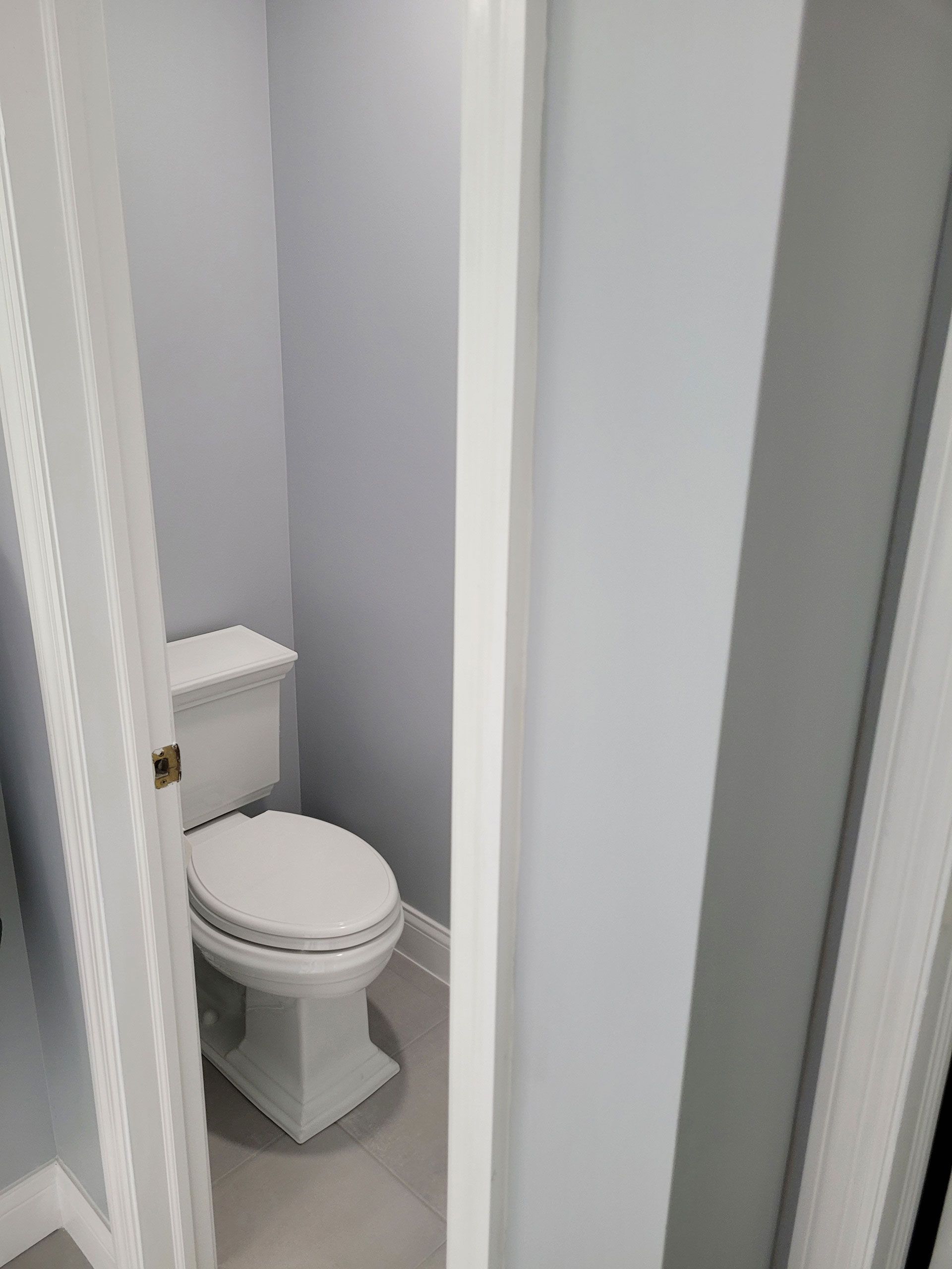 A small, light-blue painted bathroom with a white toilet. The door frame is white.