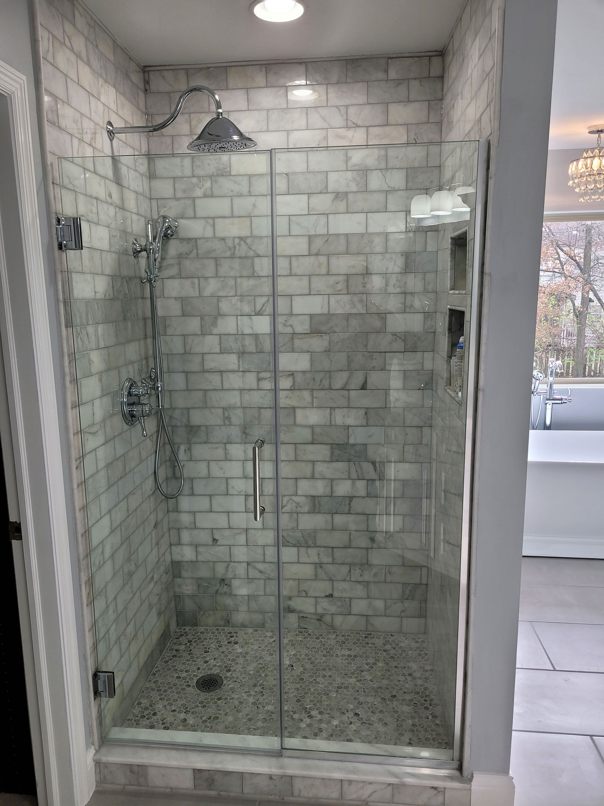 Shower with marble-look brick tiles, glass door, and pebble floor. Chrome fixtures.