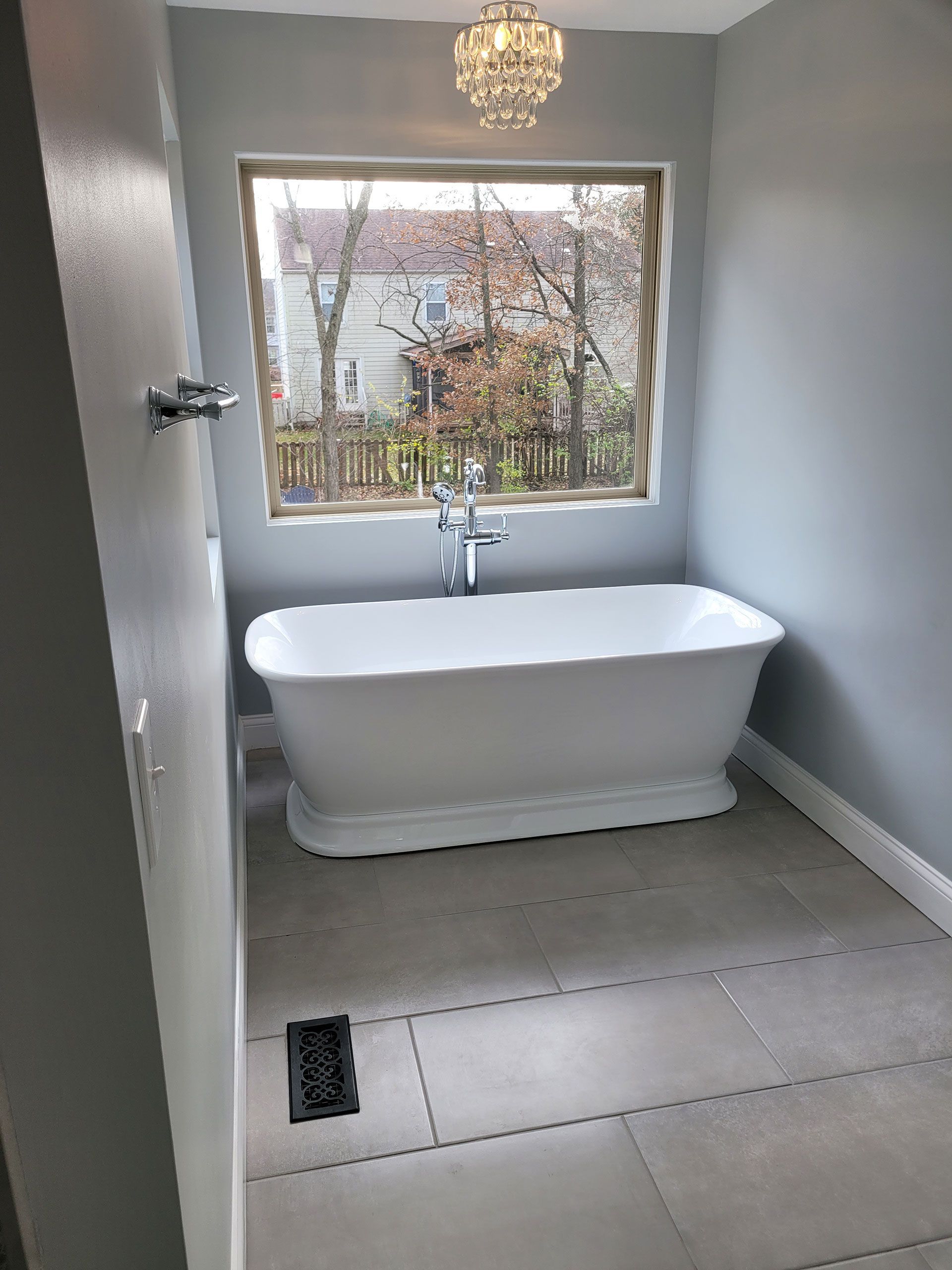 Bathroom with a white freestanding tub by a window, gray tile floor, and light blue walls.