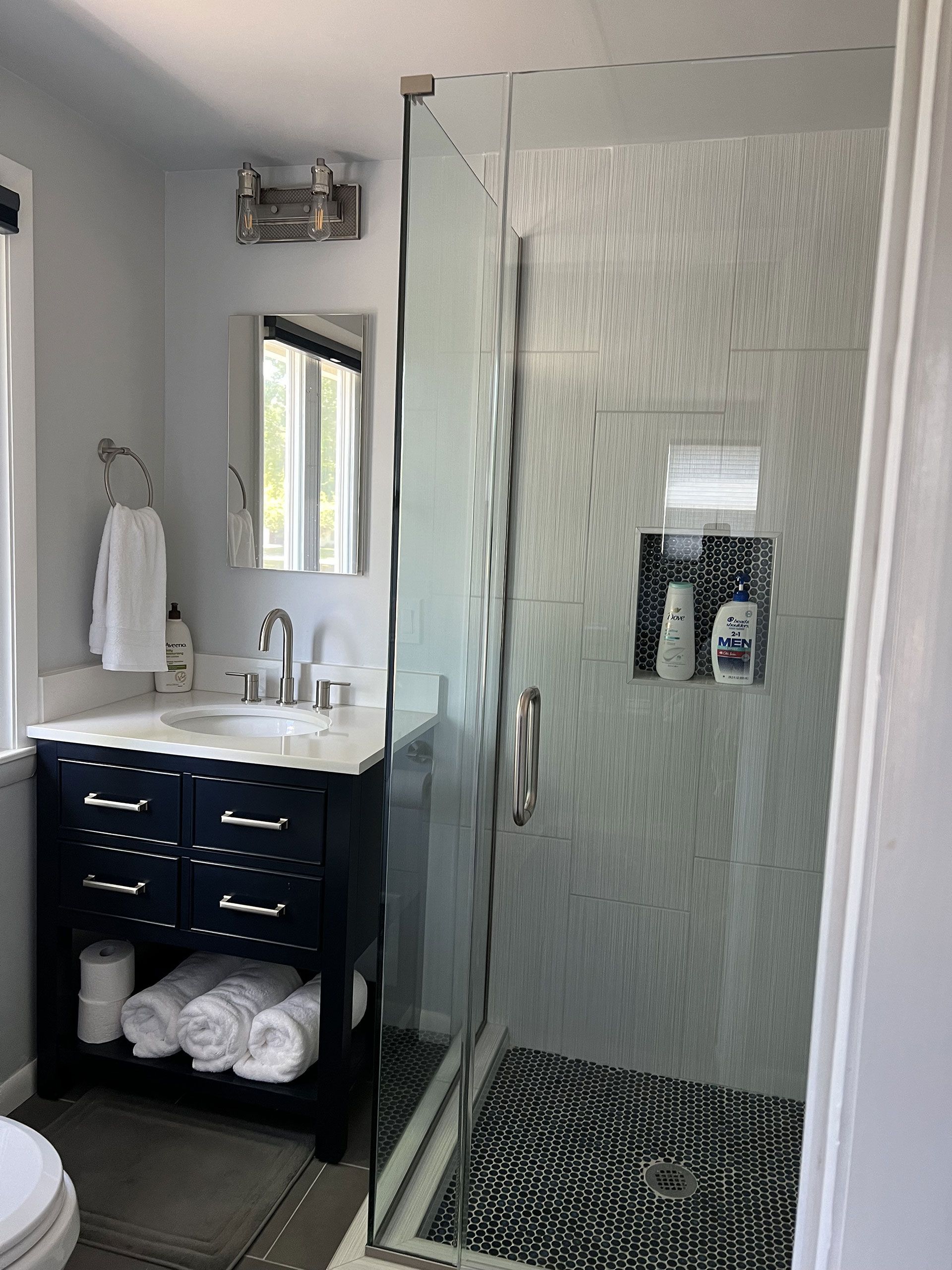 Bathroom with navy vanity, glass shower, and patterned tile floor.