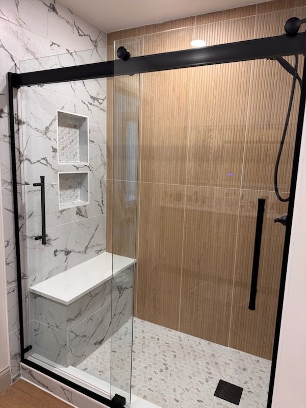 Modern shower with marble and wood-look tile, black frame, glass door, built-in bench, and niche.