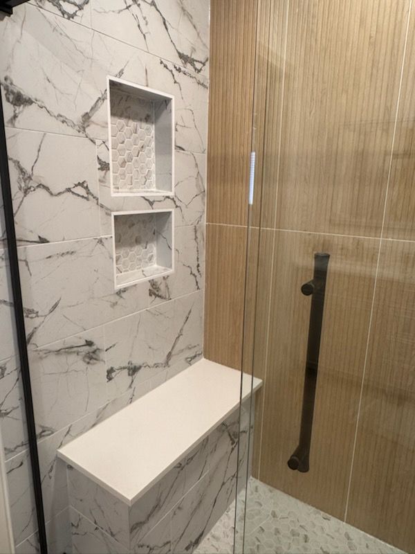 Shower with marble-look tile, built-in bench, and glass door. Includes two built-in shelves and a wood-look tile wall.