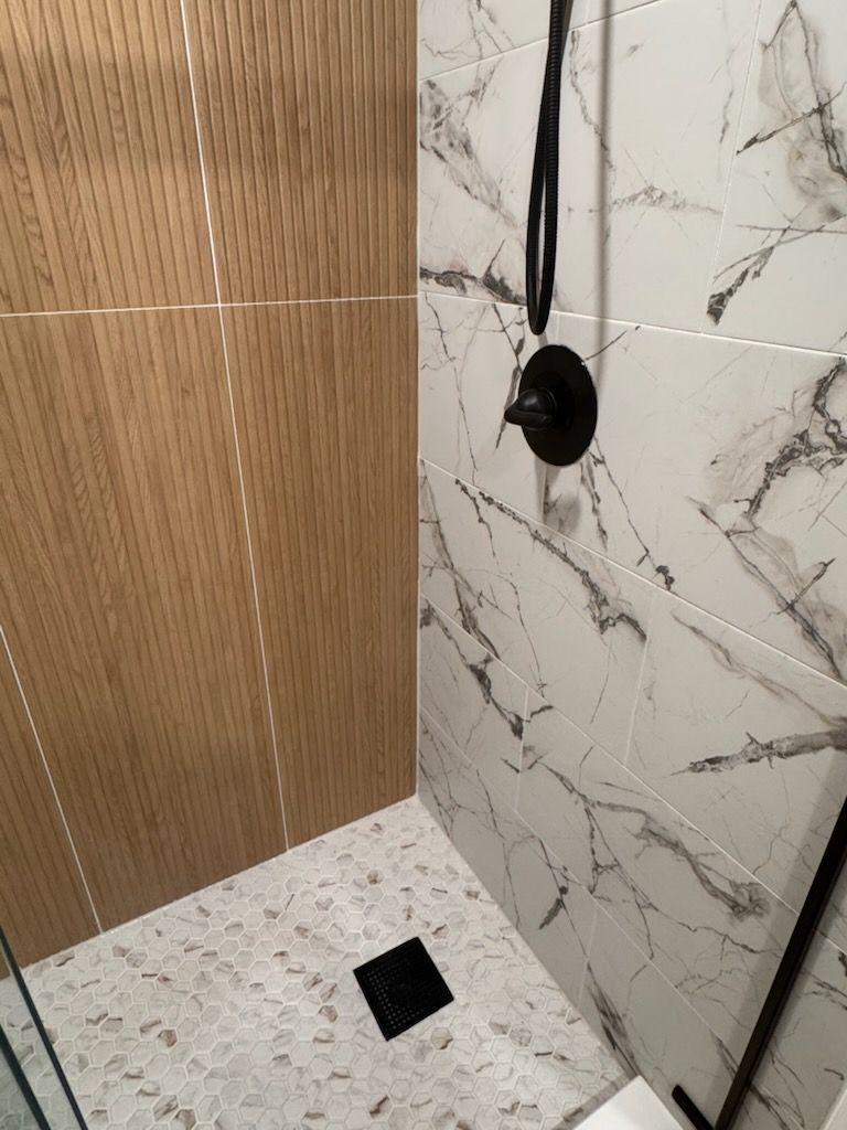 Shower with marble-patterned tiles and wood paneling. Black showerhead and floor drain.