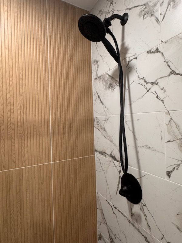 Black showerhead and wand against marble and wood-paneled shower walls.