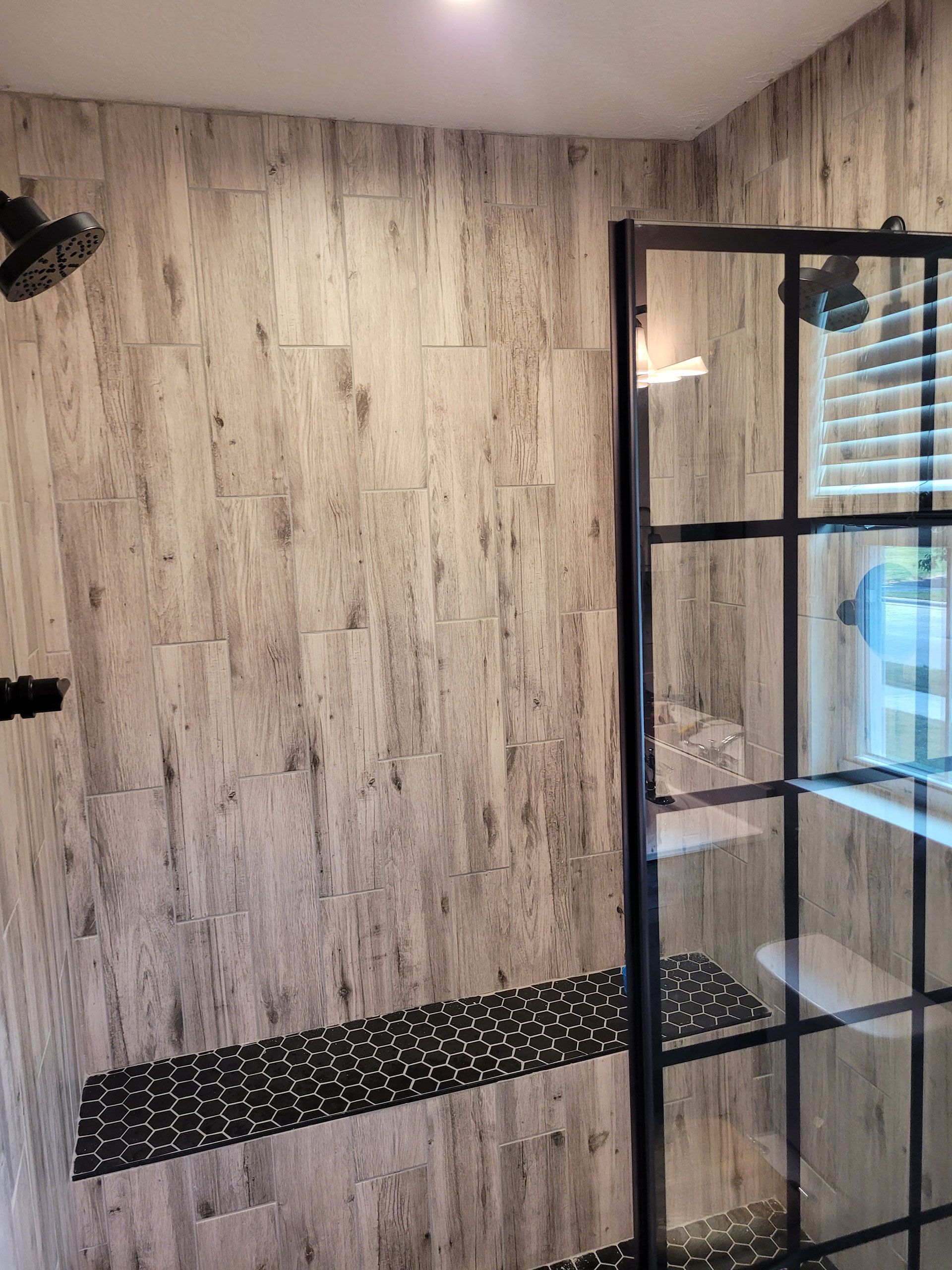 Shower with wood-look tile walls, black pebble floor, and glass enclosure with black metal frame.