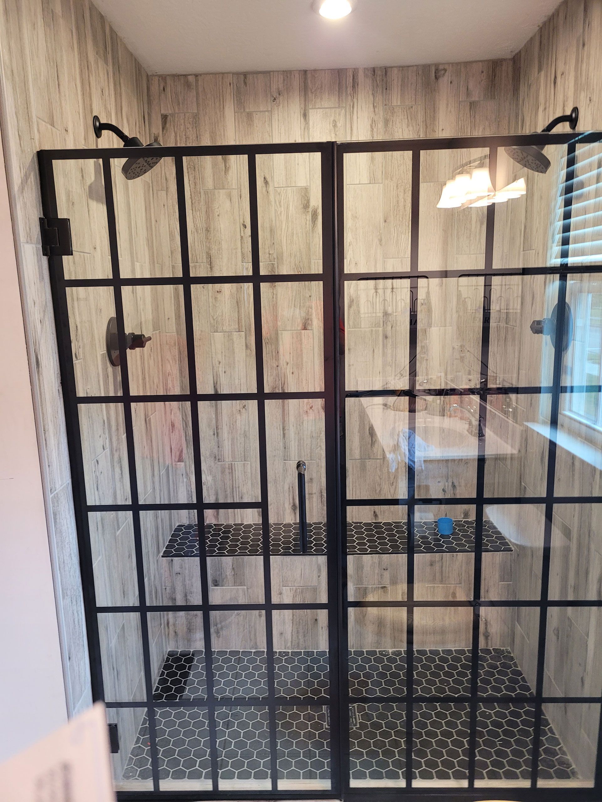 Shower with black framed glass doors, two shower heads, and tiled interior.