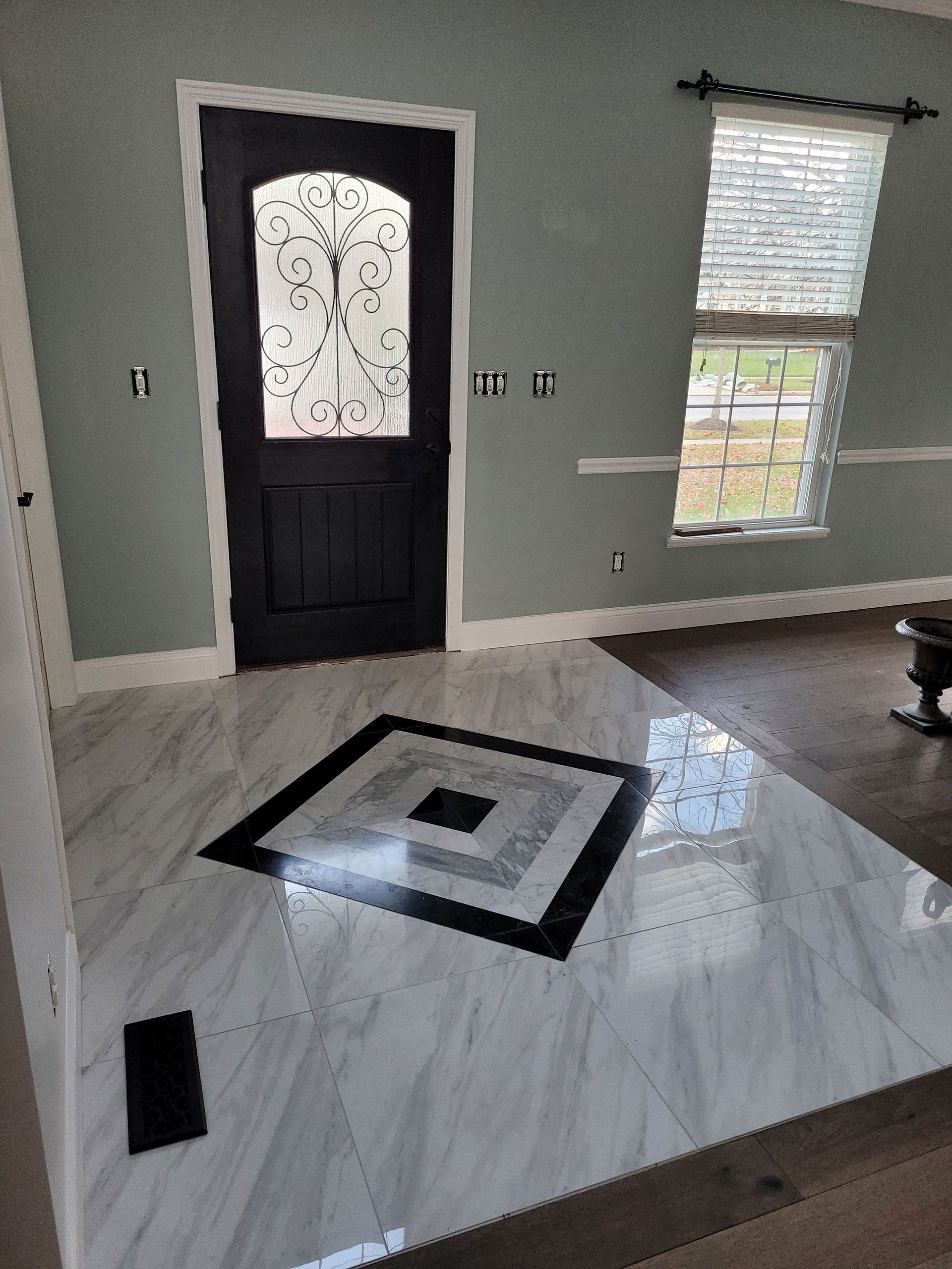 Entryway with light gray walls, dark door with ornate glass, and patterned tile floor.