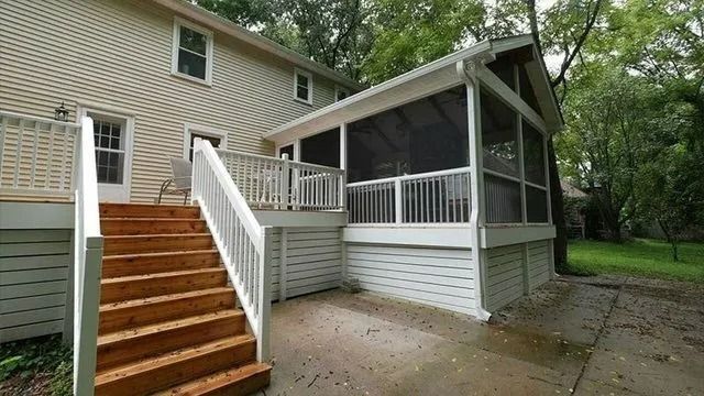 Back of a two-story beige house with a wooden deck, stairs, and a screened-in porch.