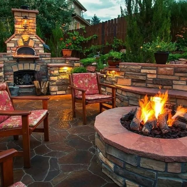 Stone patio with outdoor fireplace and pizza oven, seating area, and fire pit with flames.