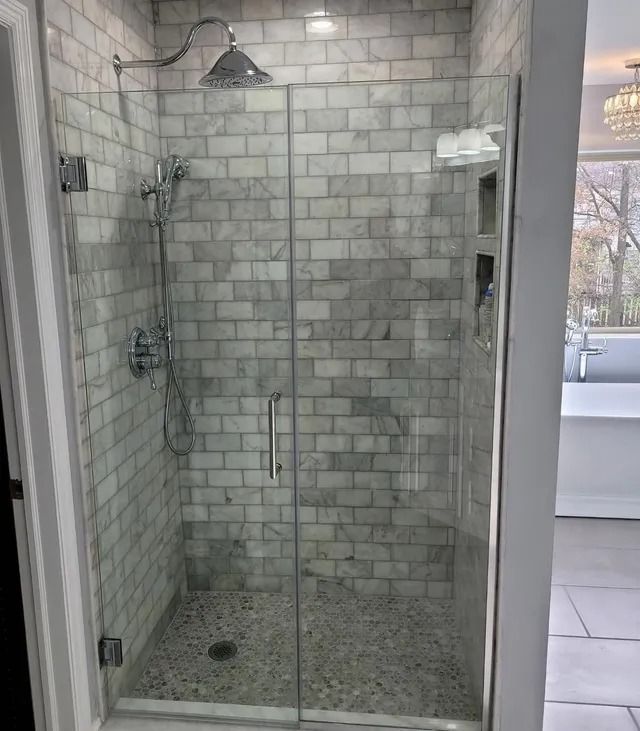 Marble-tiled shower with a clear glass door. Pebble floor and silver fixtures.