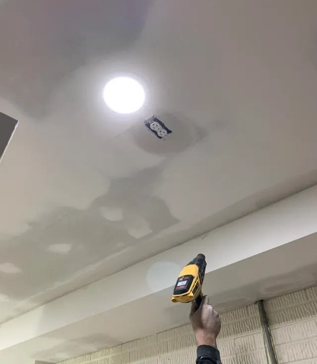 Person uses heat gun on ceiling with recessed light and patched hole.