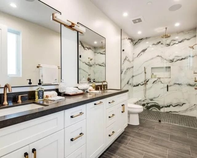 Luxurious white bathroom with marble shower, double vanity, and brass fixtures.