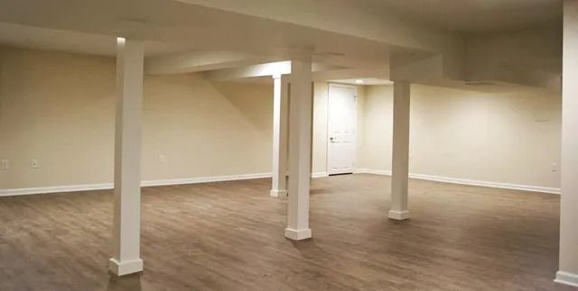 Basement interior with support pillars, neutral walls, and wood-look flooring.