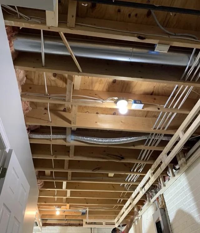 Open ceiling with exposed wooden beams, ducts, and wiring in a basement.
