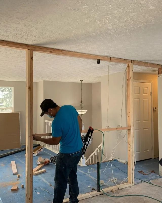 A person in a blue shirt constructs a wood frame for a wall in a room.