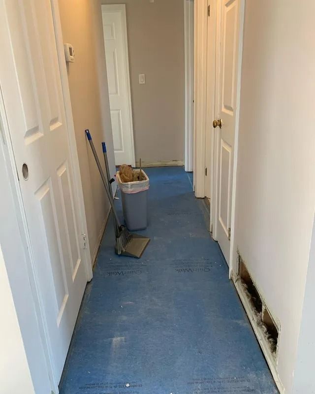 Hallway under construction with blue flooring, doors, and debris.