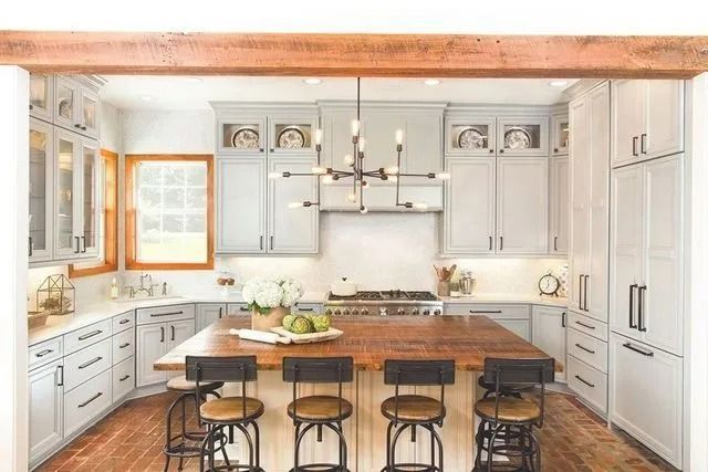 Light gray kitchen with wood island, cabinetry, and flooring. Stainless steel appliances and a modern chandelier.