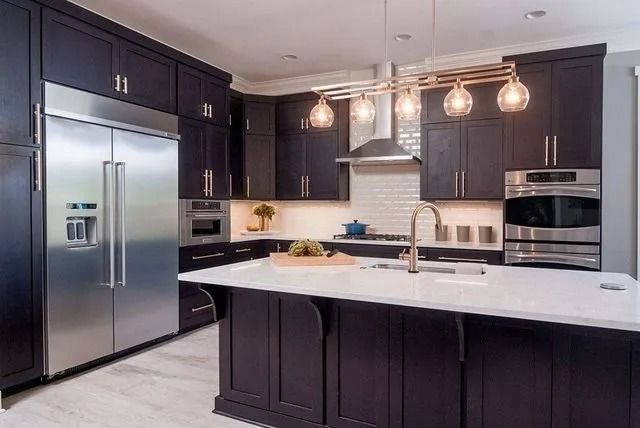 Modern kitchen with dark cabinetry, stainless steel appliances, and a white island.