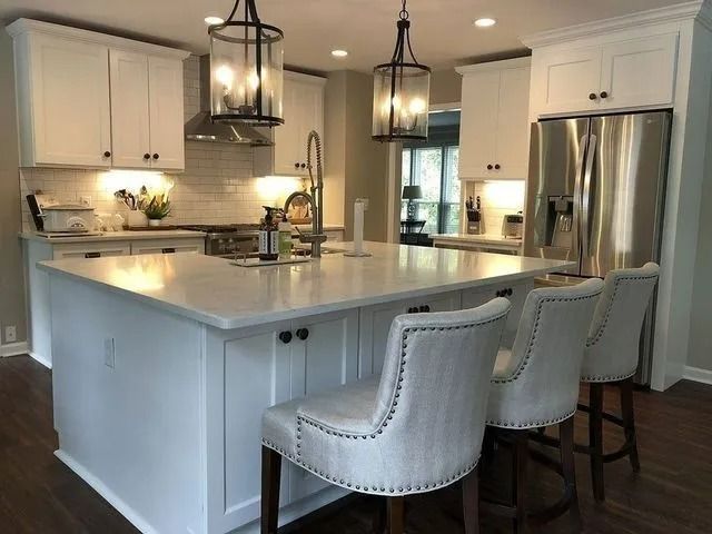 White kitchen with island, pendant lights, stainless steel appliances, and upholstered bar stools.