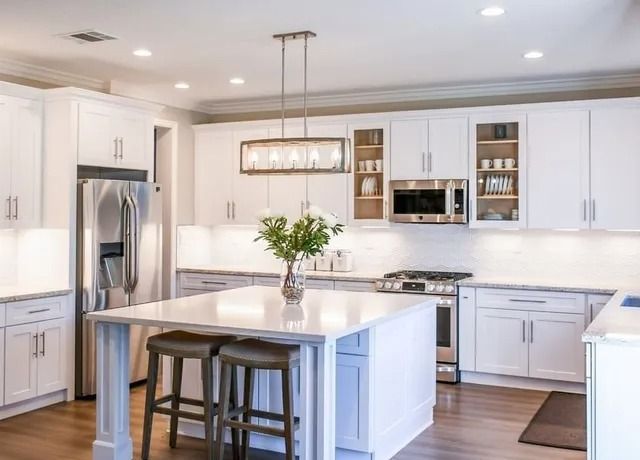 Bright white kitchen with stainless steel appliances, white island, and wooden floors.