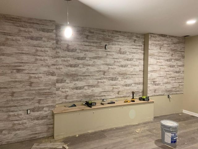 Interior wall with faux wood paneling under construction, unfinished drywall, tools on a bench.