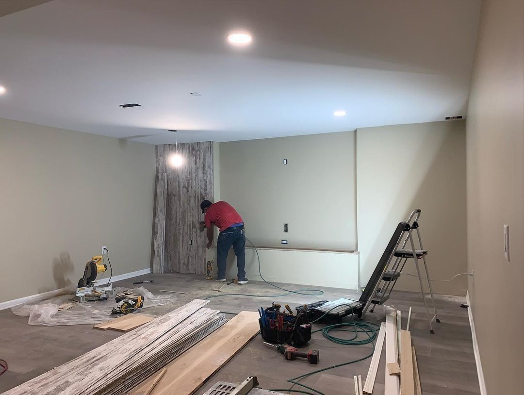A person installing wood paneling on a wall in a room under construction.