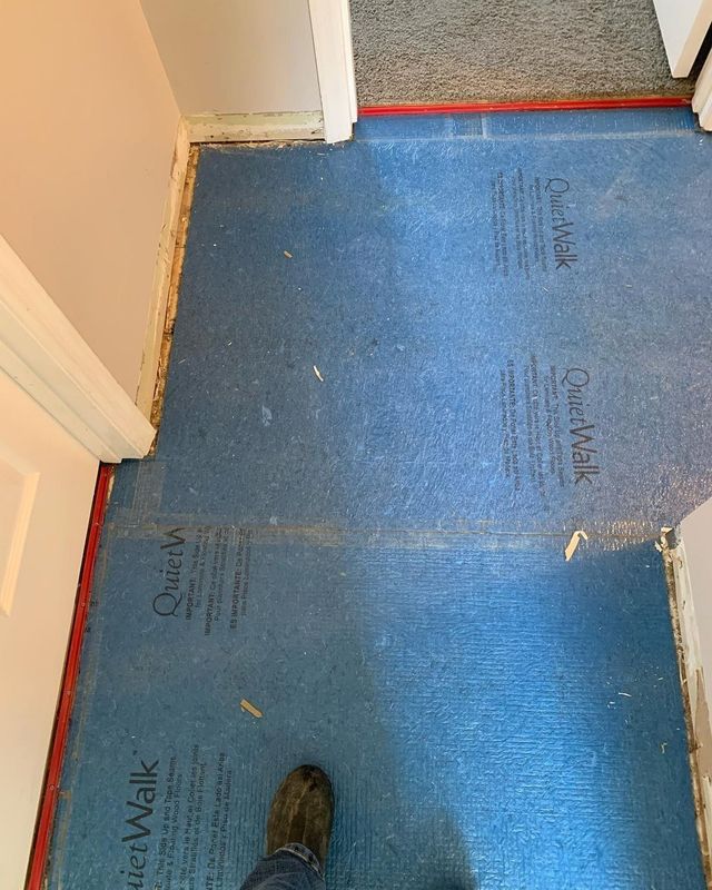 Blue flooring underlayment in a doorway, next to a doorway frame. A foot is visible.