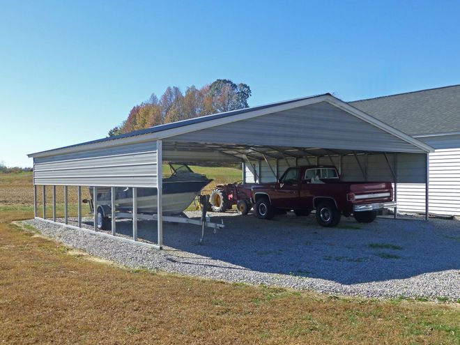 Metal carport with a red pickup truck and a smaller vehicle on a gravel driveway beside a house.