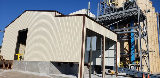 Industrial building with beige siding and metal framework beside a larger plant structure