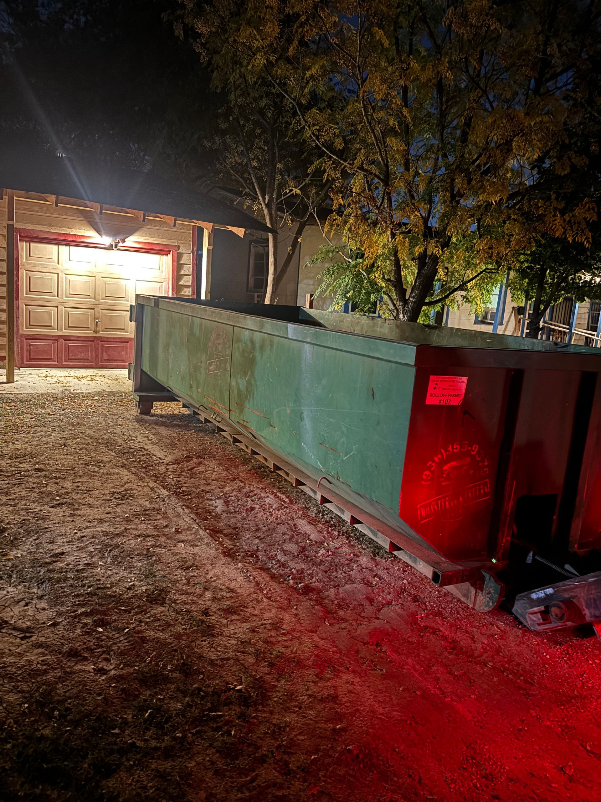 A long green dumpster in front of a building with warm lighting at night.