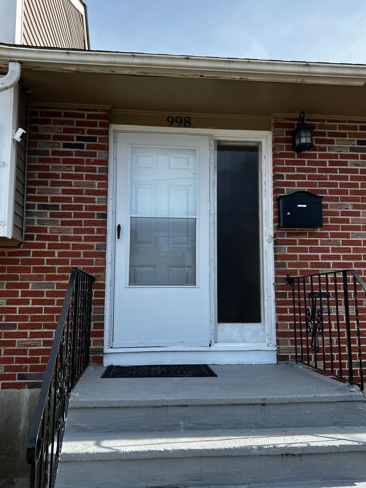 White door with sidelight on a brick house; black mailbox and steps.