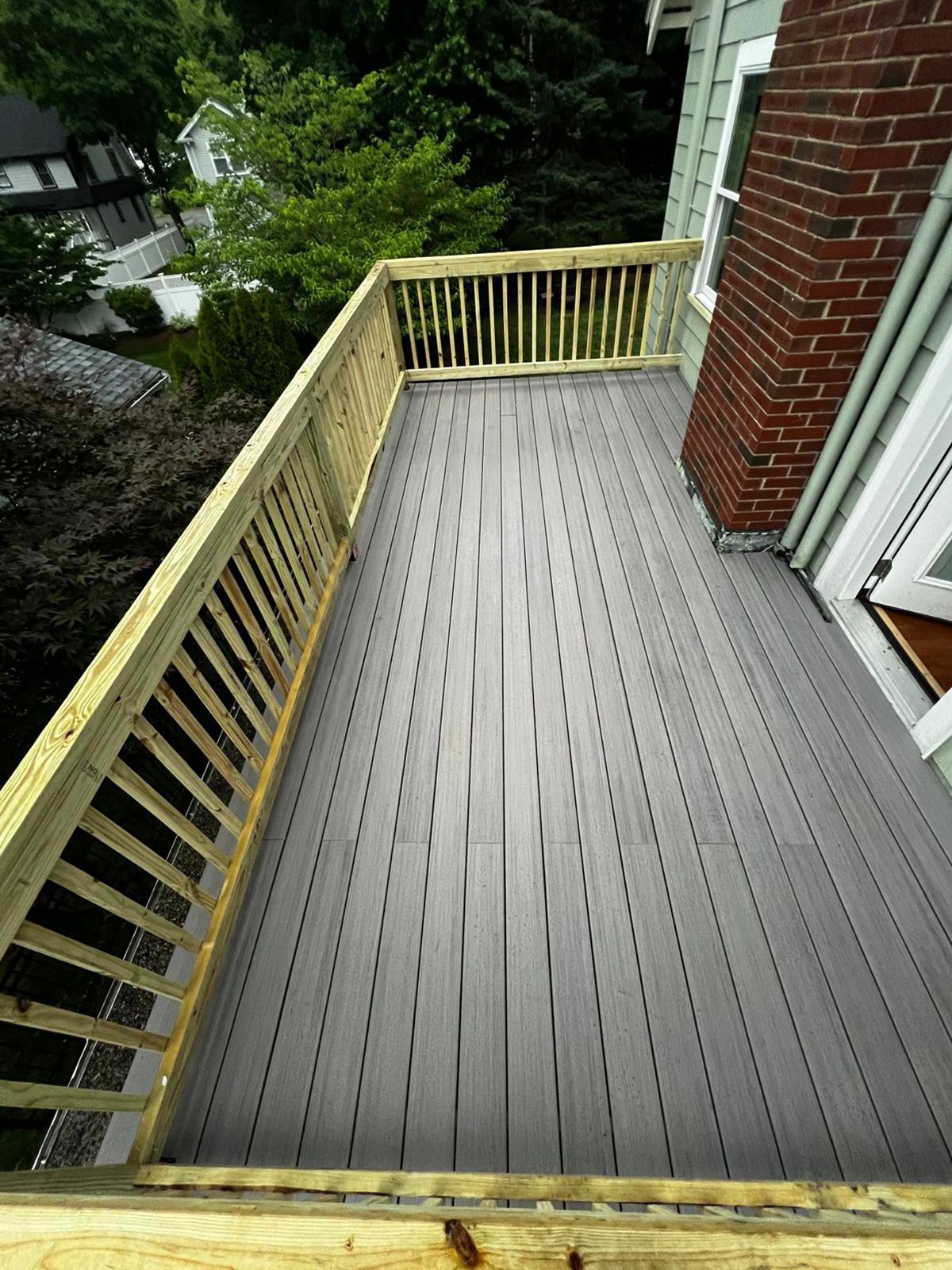Gray deck with wood railing attached to a building with brick chimney.