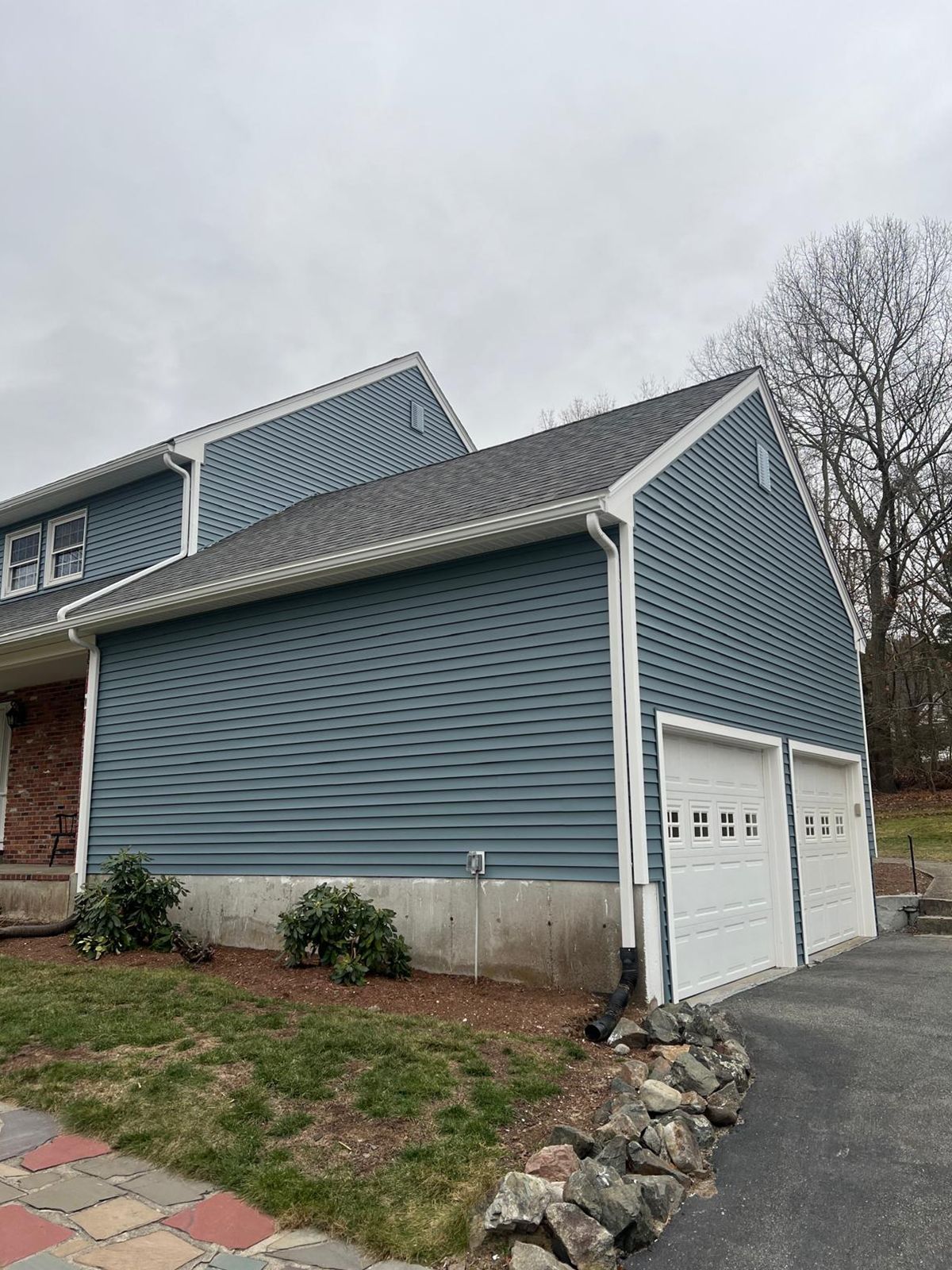Blue sided house with white garage doors and a grey roof under an overcast sky.