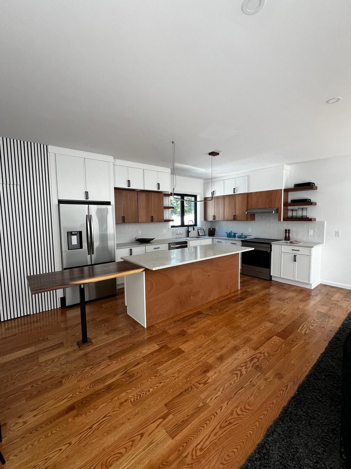 Modern kitchen with wooden floors, white and wood cabinets, stainless steel appliances, and a central island.