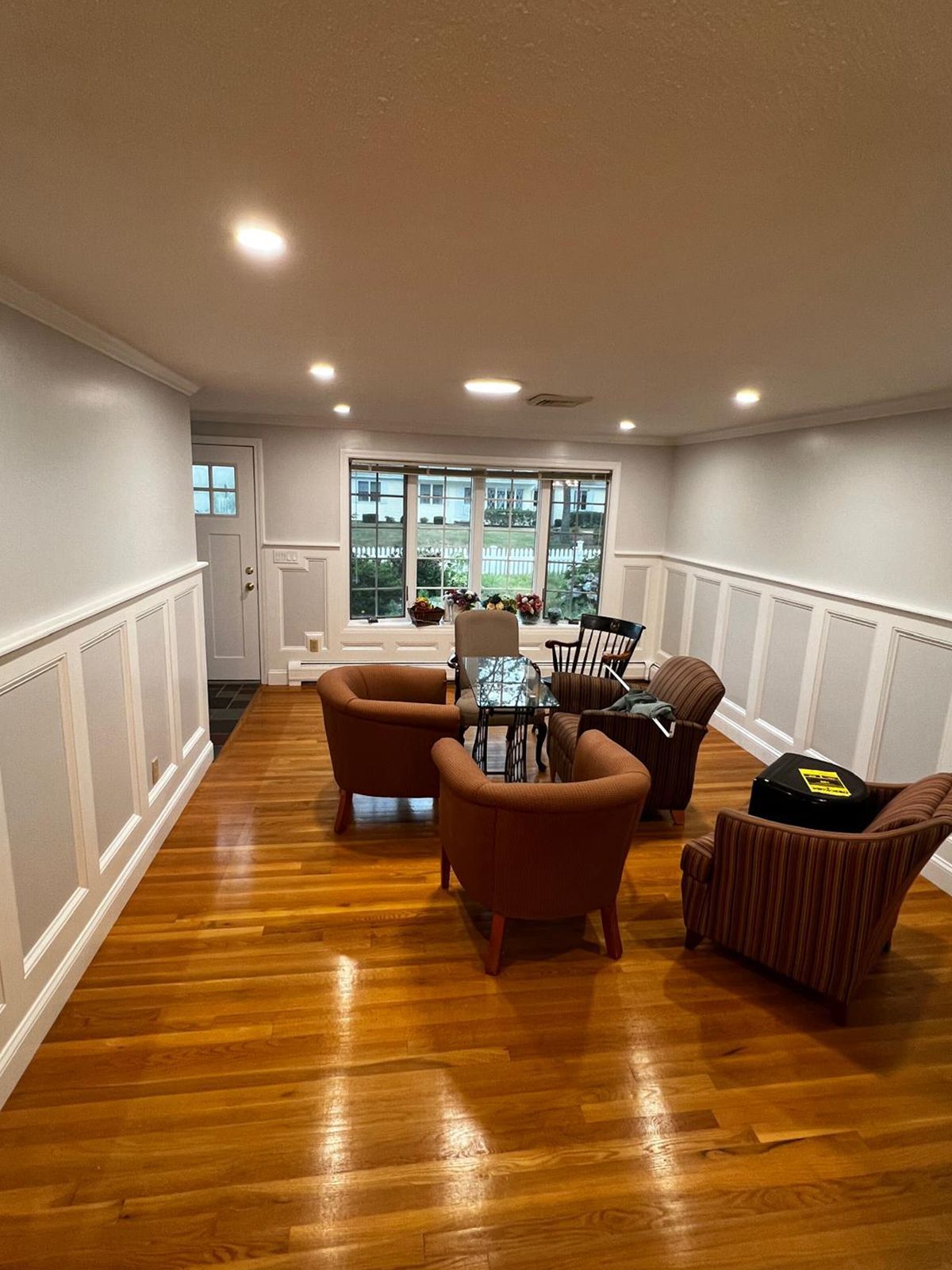 Living room with wood floors, paneled walls, and several armchairs arranged around a small table.