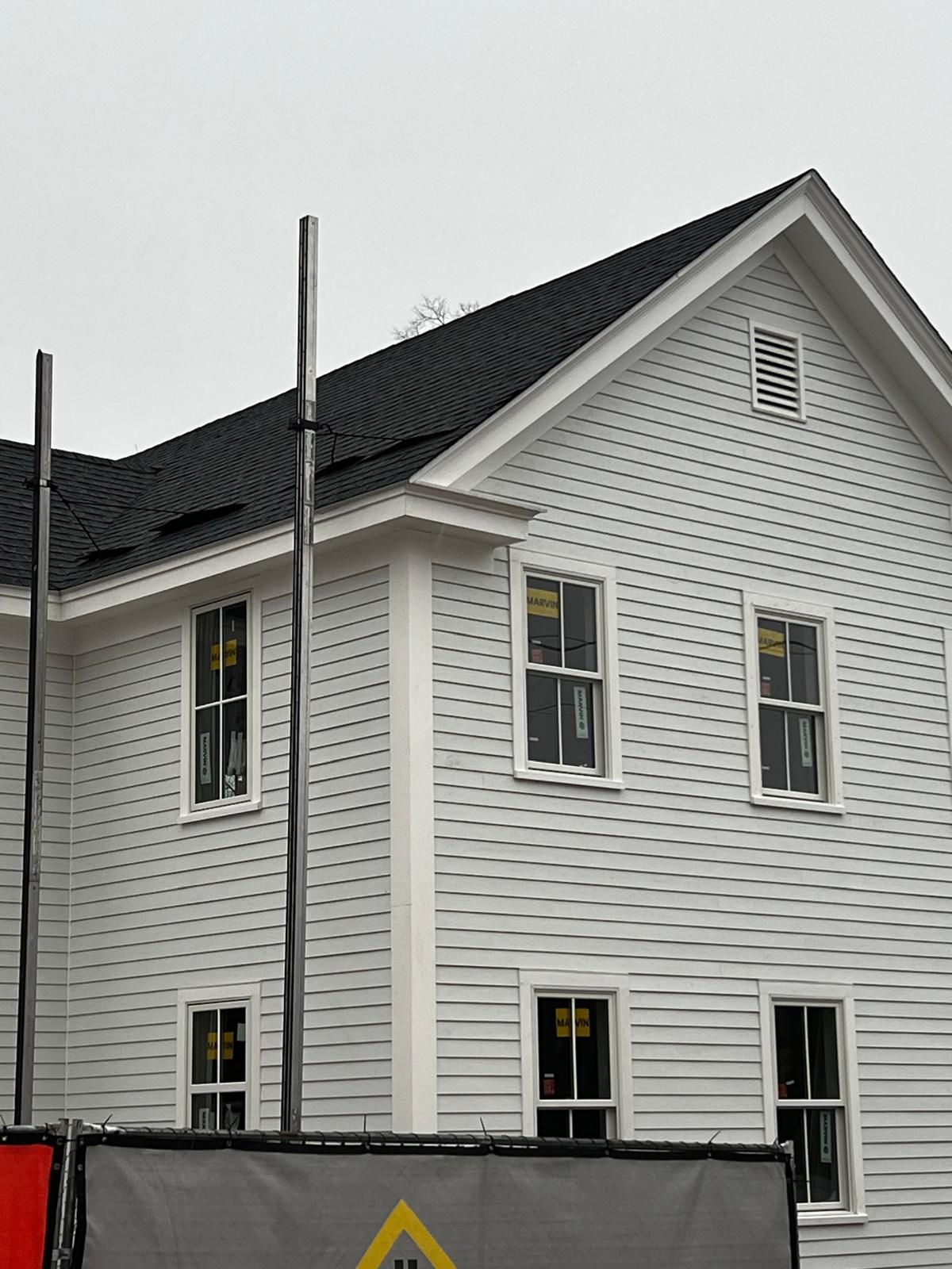 White clapboard house under construction, with windows and dark roof.