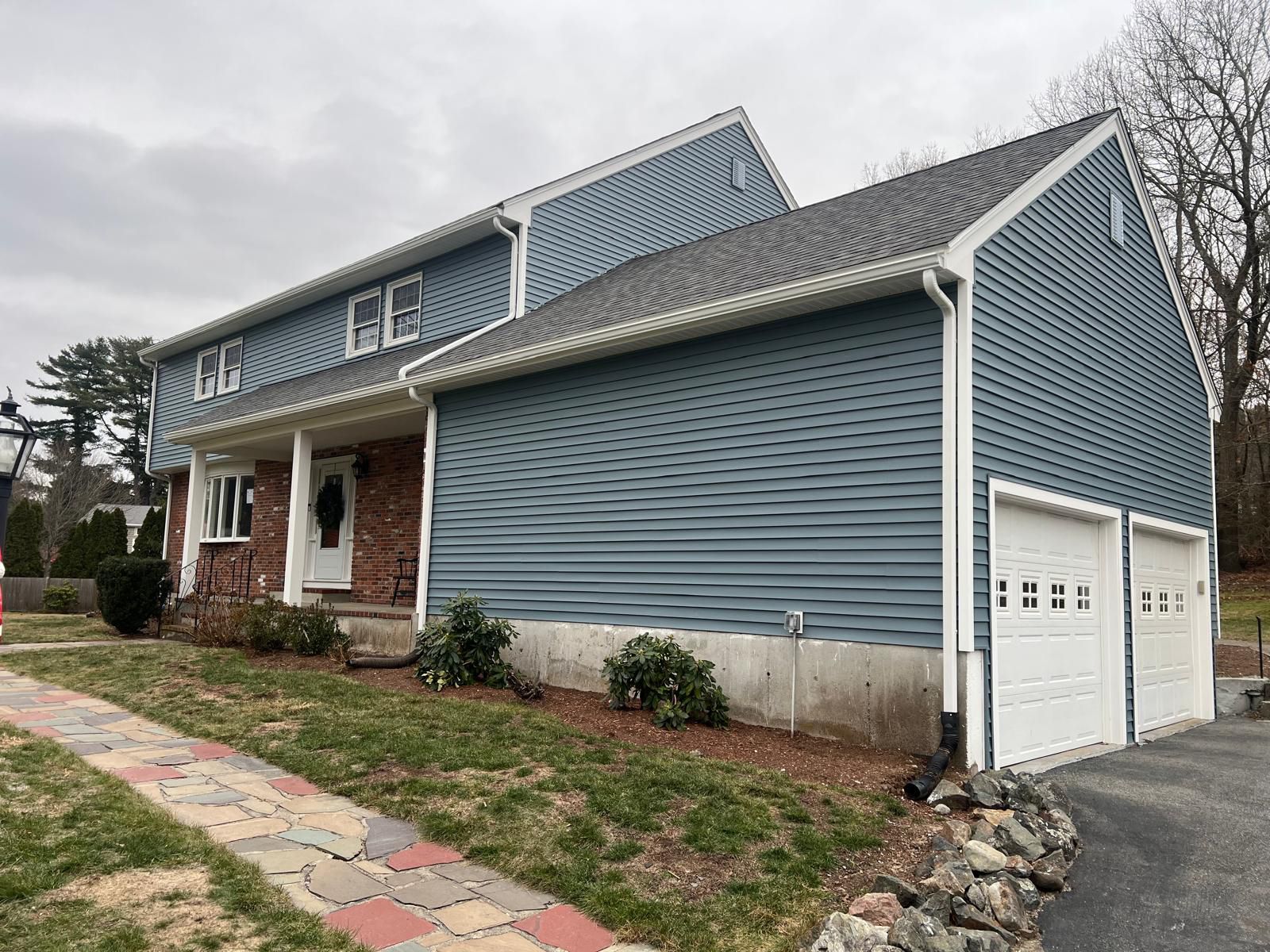 Two-story blue-sided house with a red brick front, two-car garage, and a paved walkway.