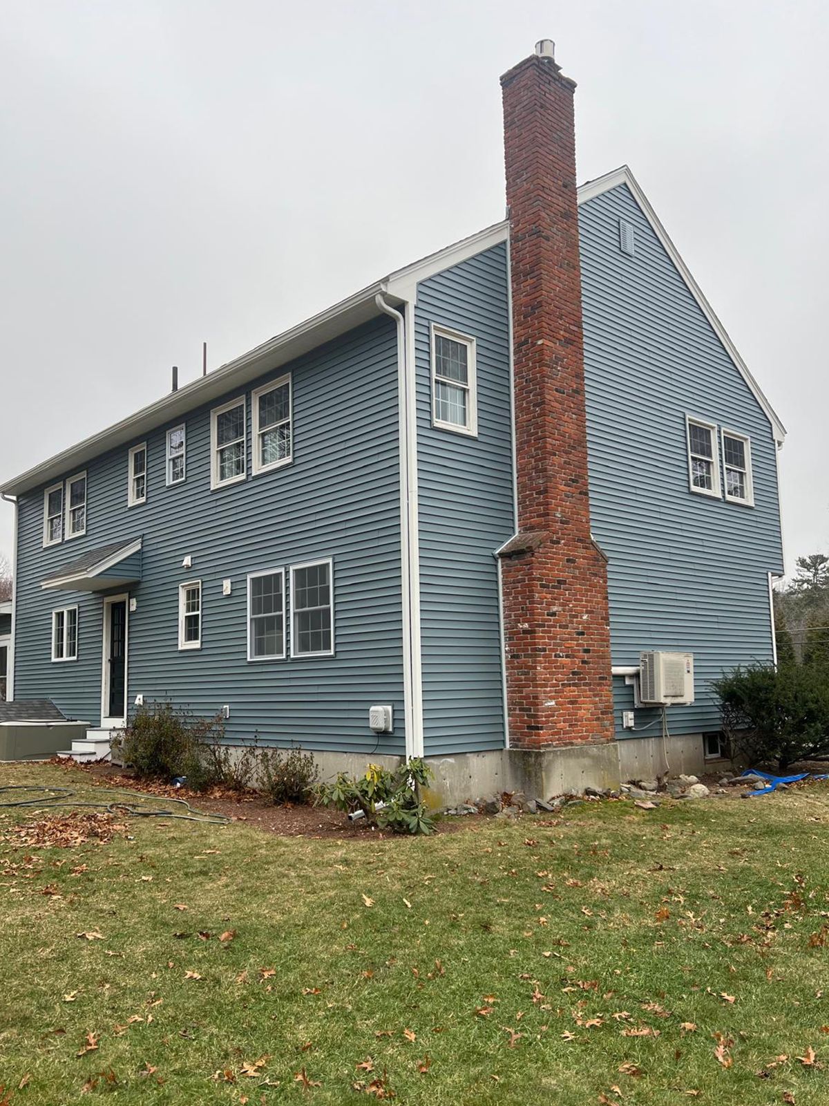 Blue sided house with brick chimney on a cloudy day.