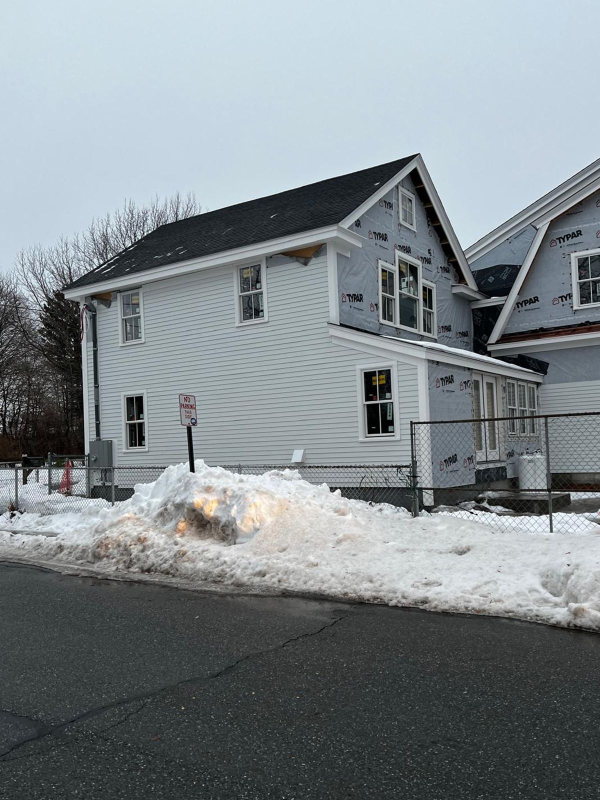 Two-story house under construction with light-colored siding, snow on the ground, and overcast sky.