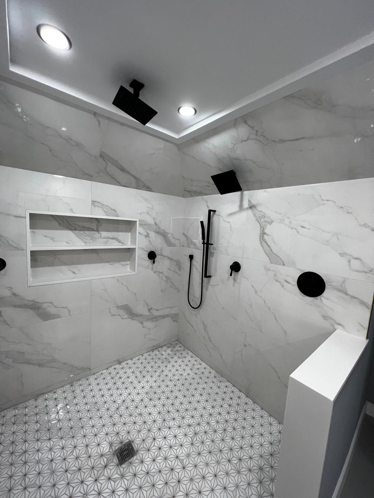 Modern shower with marble tile walls, black fixtures, and patterned floor.