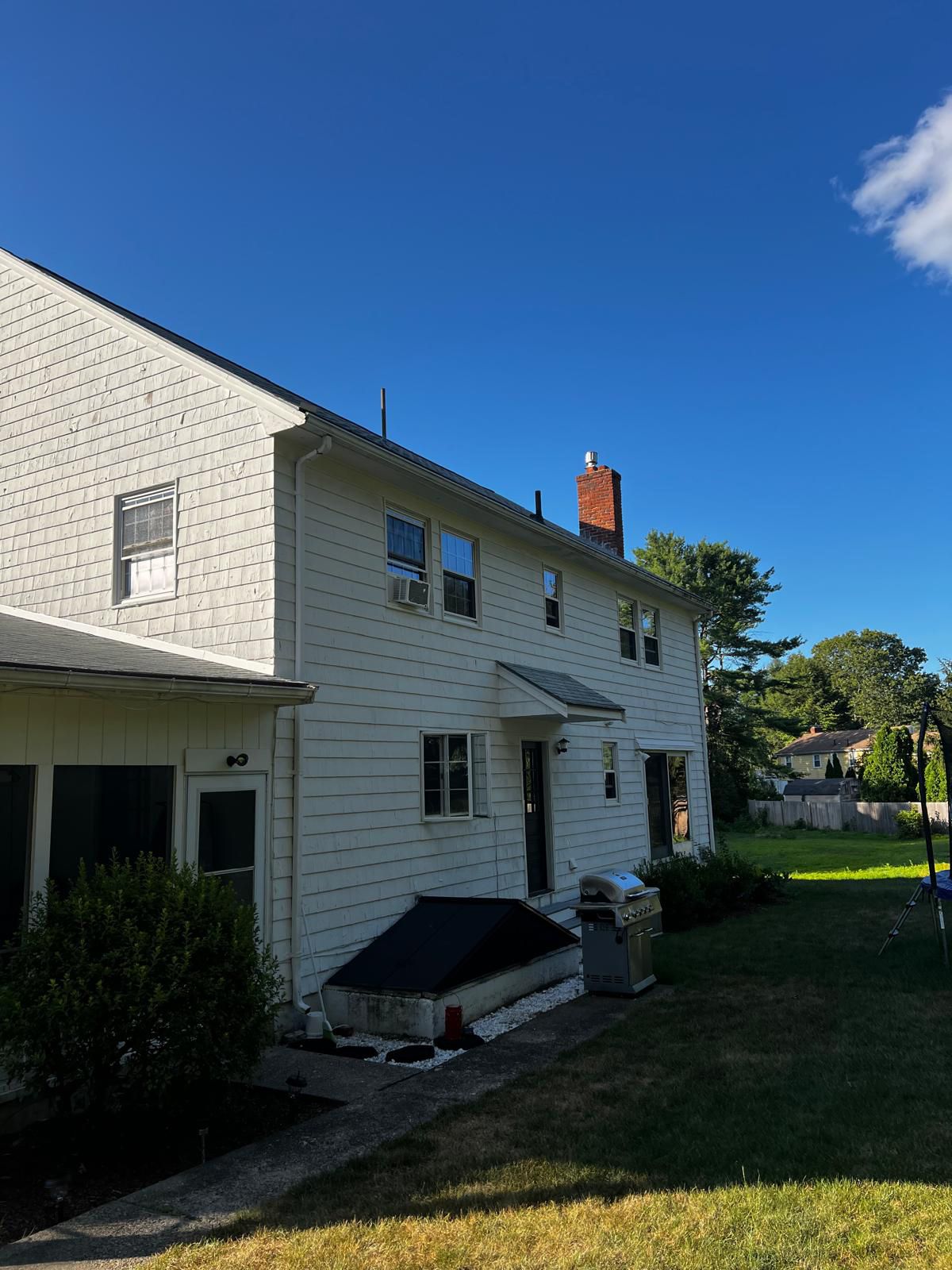 White house exterior with blue sky. Features windows, a chimney, and a barbecue grill on a lawn.